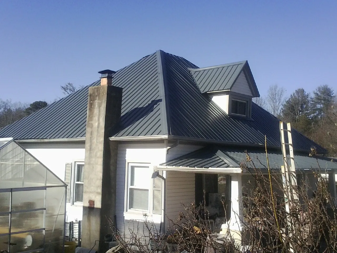 Dark blue standing seam metal roof on a white farmhouse with dormer — Slate & Tile Roof Repair by Roofing Brothers in Polkville