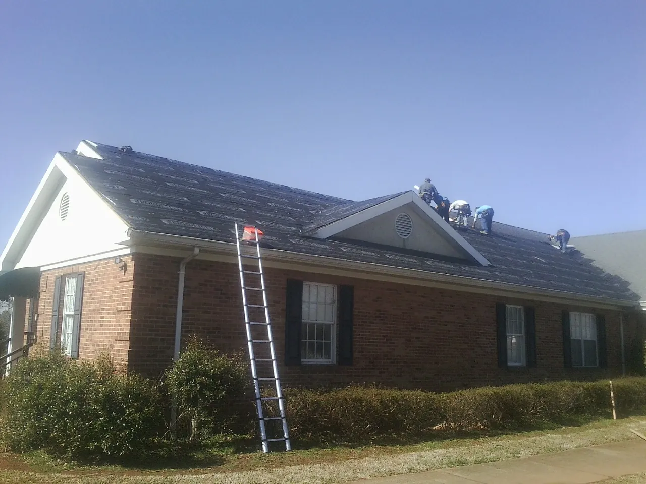 Crew tearing shingles off a brick ranch roof with a ladder set — Emergency Roof Repair work by our crew in Polkville