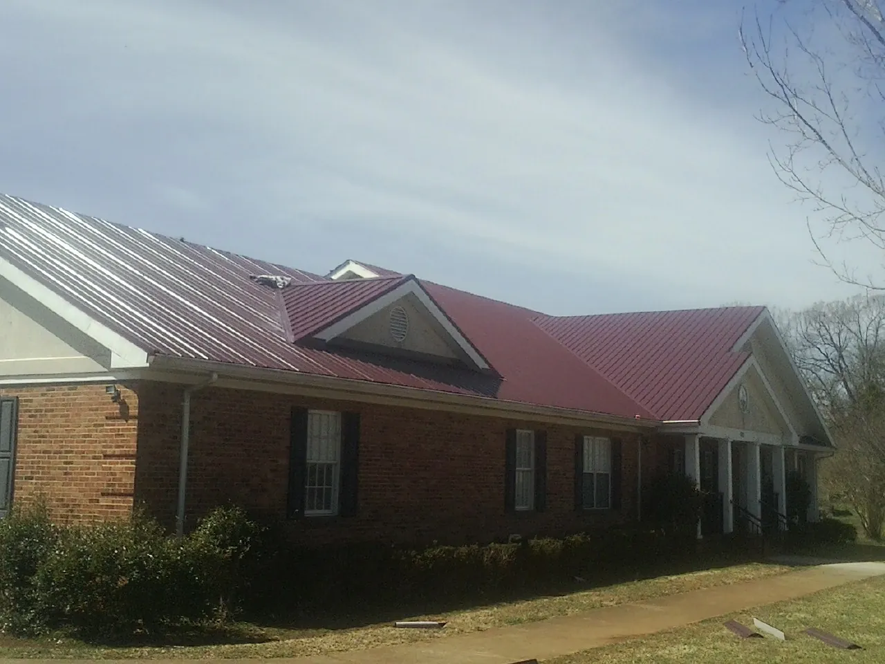 Red metal roof with gabled entries on a long brick building, from a Hail Damage Roof Repair job in Polkville