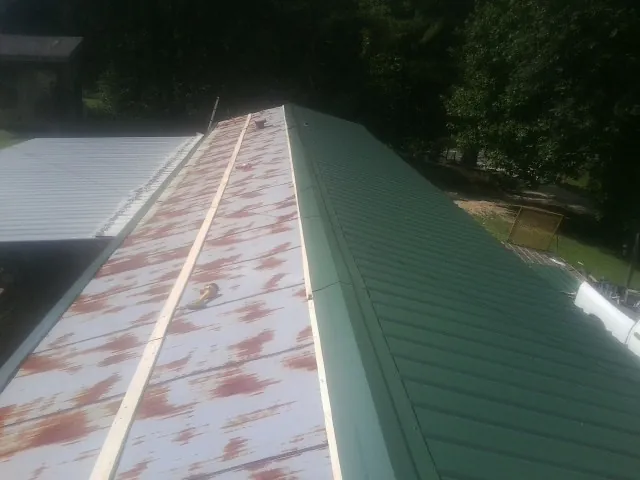 Old rusted panels beside newly installed green metal roofing — Wind Damage Roof Repair by Roofing Brothers in Polkville