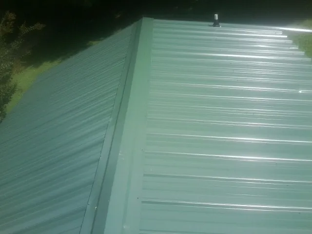 New green metal panels meeting at the ridge of a roof — Flat Roof Repair work by our crew in Polkville