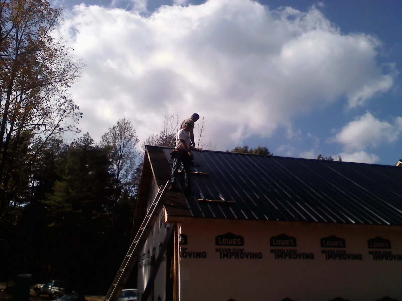 Roofer fastening dark metal panels high against a cloudy sky, from a Roof Inspection job in Polkville