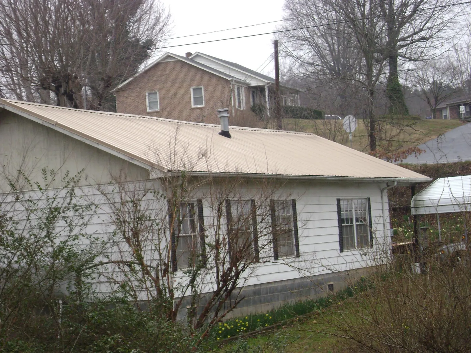Tan metal roof on a white sided house set into a hillside — Commercial Roofing by Roofing Brothers in Polkville
