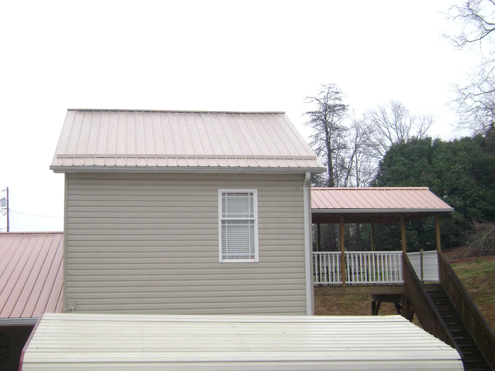 Tan metal roofs on a two story addition and attached porch, from a Roof Replacement job in Polkville
